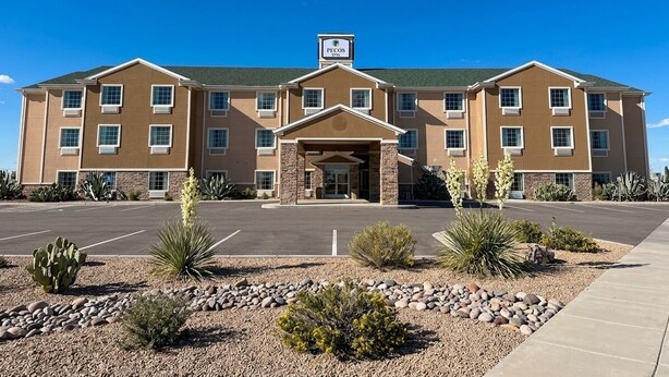 A multi-story hotel with a central entrance, parking lot, and landscaped garden with desert plants. - Pecos Inn (Pecos)