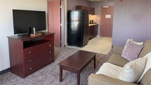 A living room with a TV, a coffee table, a sofa, and a kitchen area with a refrigerator. - Pecos Inn (Pecos)