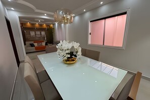 A dining area with a white table, a chandelier, and a window with pink curtains.