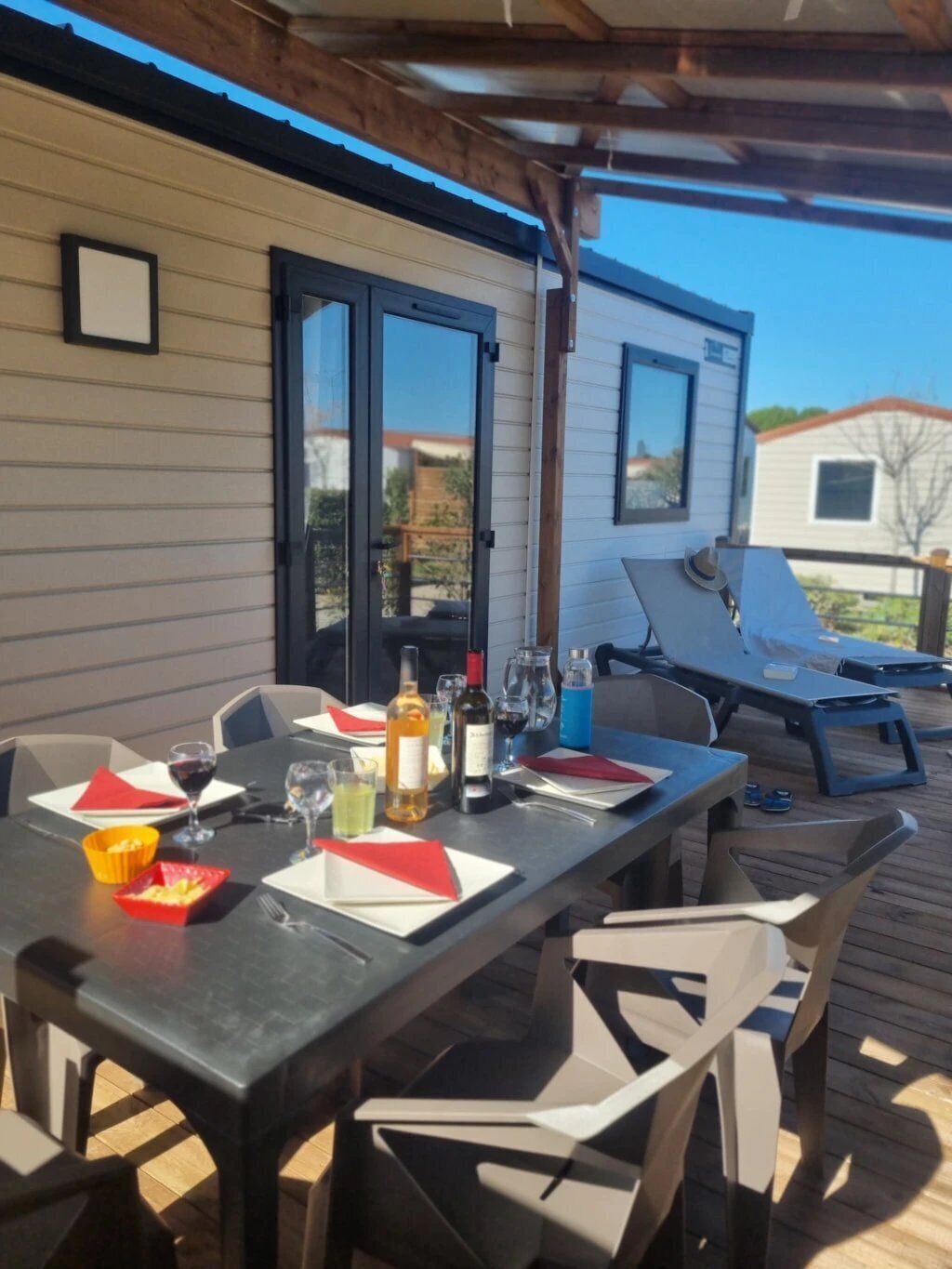Un espacio exterior para comer con una mesa lista para dos, sillas y un porche techado.