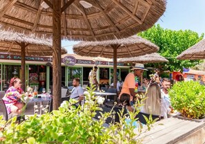 Ein Außenbereich mit Essplätzen, ausgestattet mit Strohdächern, Tischen und Stühlen.