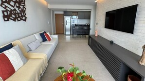 Ein modernes Wohnzimmer mit einer Couch, einem Flachbildfernseher und einer Küche im Hintergrund.