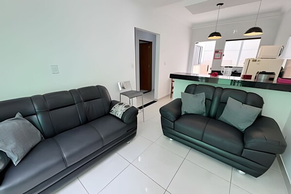 A living room with two black sofas, a dining table, and a kitchen area with cabinets and a countertop.