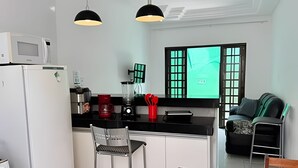 Et moderne køkken med køleskab, mikrobølgeovn, kaffemaskine og blender. Der er en bar med en stol og en sofa.