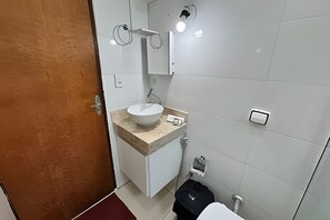 A bathroom with a white sink, a mirror, a towel rack, a toilet, and a door. - Simple and Functional House in Araxá (Araxá)