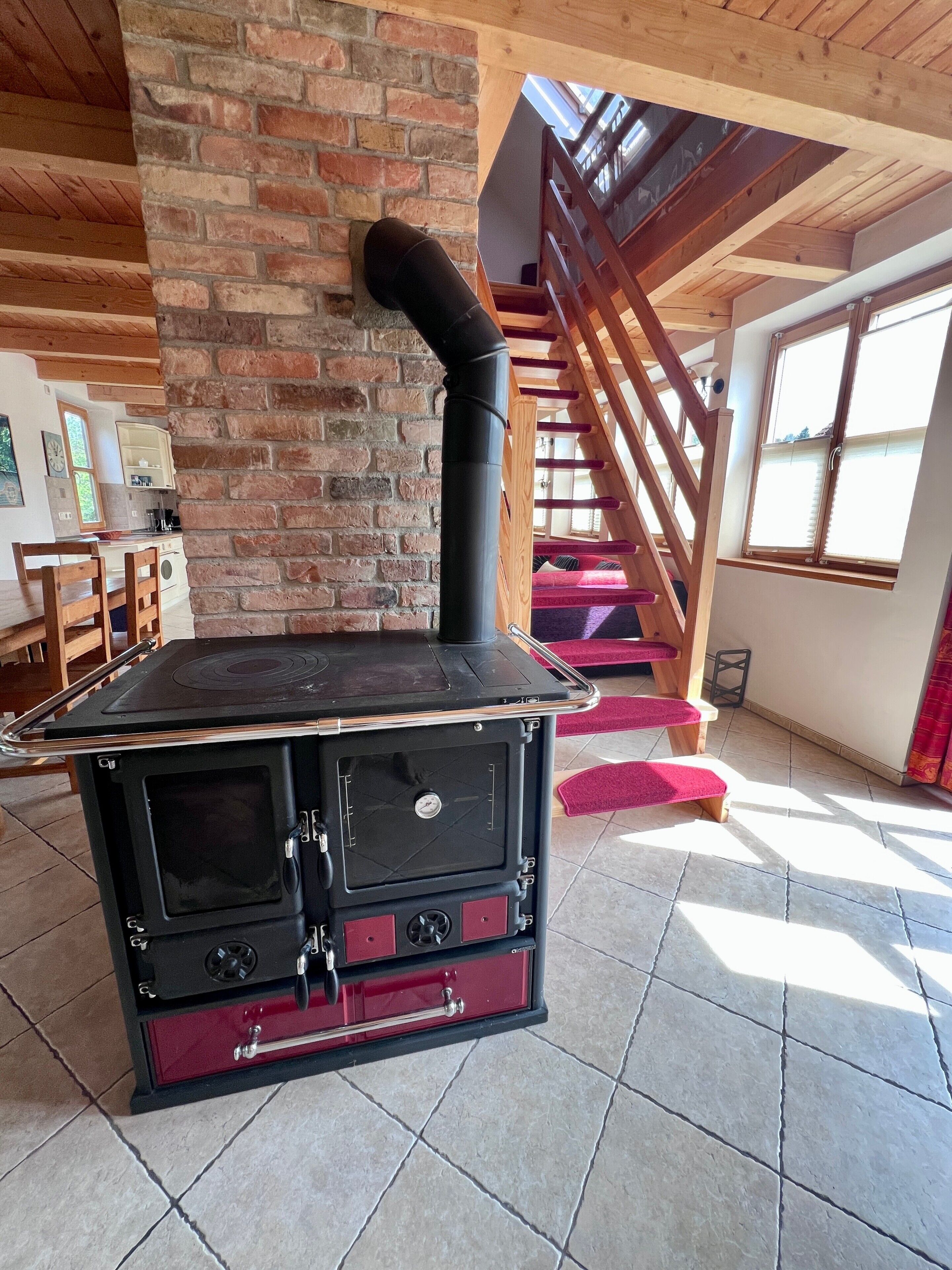 A room with a brick wall, a black stove, a wooden staircase, and a window.