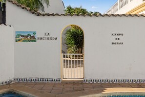 Un espace piscine bordé de carreaux, avec une porte et un mur orné d’une inscription et d’une petite peinture.