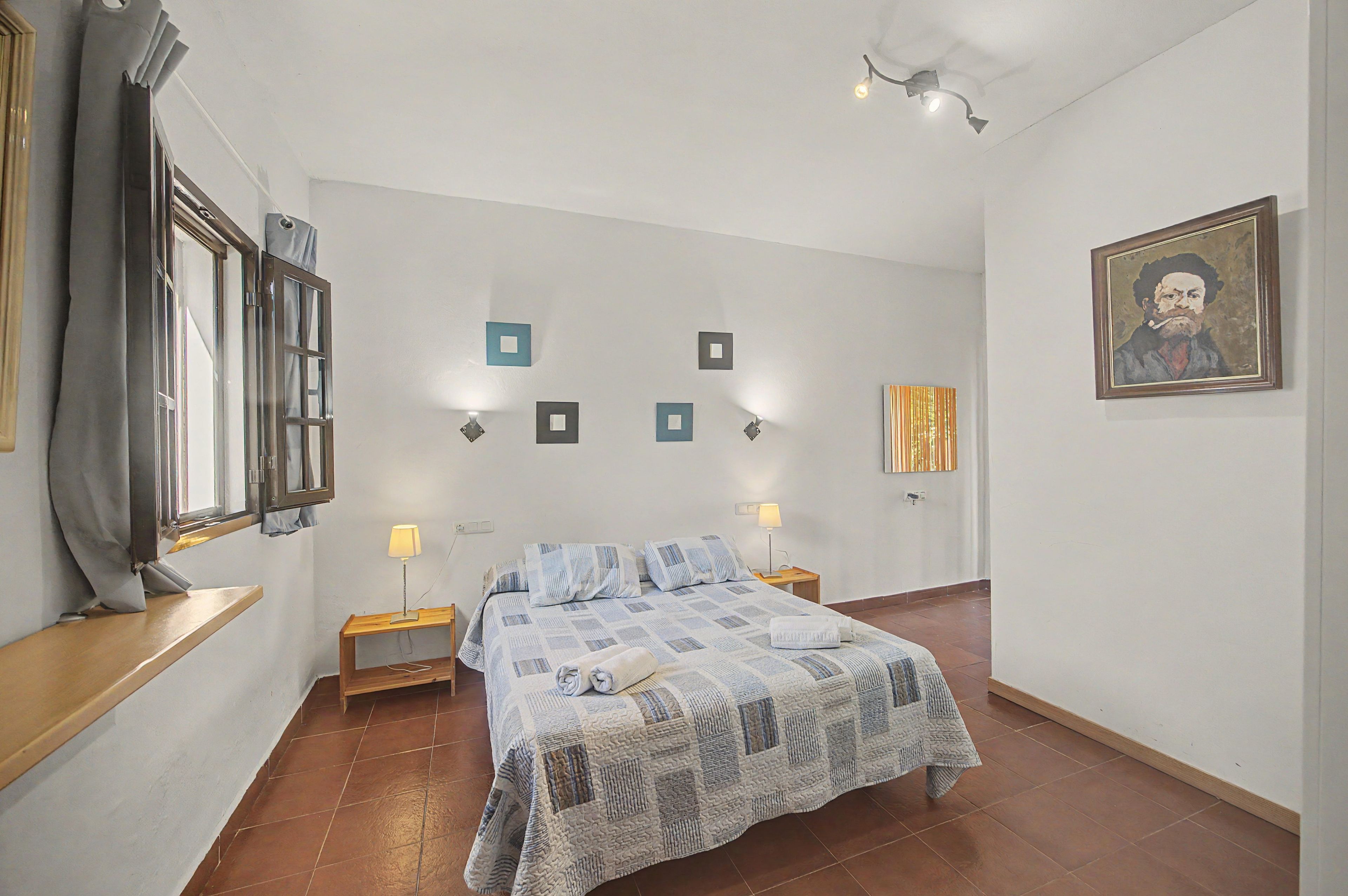 Une chambre à coucher avec un lit, des lampes de chevet, une fenêtre avec des rideaux et des interrupteurs d’éclairage fixés au mur.