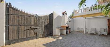 A gated courtyard with a barbecue area, outdoor seating, and a white wall with decorative elements.