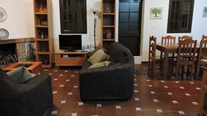 A living room with a sofa, television, and a dining area with chairs and a table. - Country House 'La Hacienda Campo De Borja' with Private Pool, Wi-Fi & Air Conditioning (Conil de la Frontera)