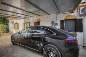 Une voiture noire est garée dans un espace de garage couvert, avec un bâtiment blanc en arrière-plan.