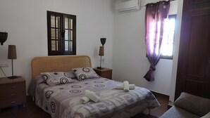 A bedroom with a bed, two bedside tables, a window with curtains, an air conditioning unit, and a door. - Country House 'La Hacienda Campo De Borja' with Private Pool, Wi-Fi & Air Conditioning (Conil de la Frontera)