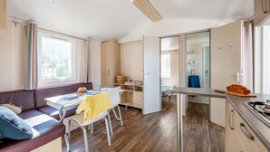 A modern kitchen with a dining area, a sofa, and a table with a yellow tablecloth. - Camping 4 étoiles - Piscine  - ccbfhbe (Badefols-sur-Dordogne)