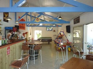 Una zona de bar con taburetes, una mesa de billar y una pantalla de televisión.