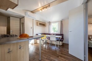 A compact kitchen with a central island, a dining area with a bench, and a window providing natural light. - Camping 4 étoiles - Piscine  - ccbfhbi (Badefols-sur-Dordogne)