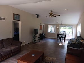 A spacious living room with a ceiling fan, a dining area with a table and chairs, and a view of the outdoors through large windows. - New Haven Woods (Wisconsin Dells)