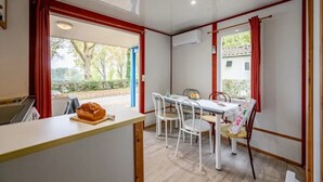 A dining area with a table and chairs, a loaf of bread on a cutting board, and a window with curtains.