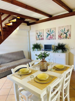 A dining area with a white table set for four, a sofa, and a kitchen area with a TV and plants. - Olbia Center-standard Apartment (Olbia)