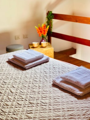 A neatly made bed with folded towels, a small table with cups and a vase of flowers, and a wooden chair in a room with a simple design. - Olbia Center-standard Apartment (Olbia)