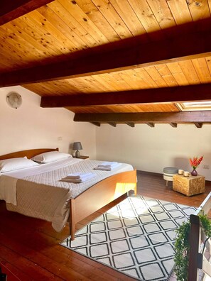 A bedroom with a wooden ceiling, a bed with white linens, a bedside table with a lamp, and a small stool with a cup and vase. - Olbia Center-standard Apartment (Olbia)
