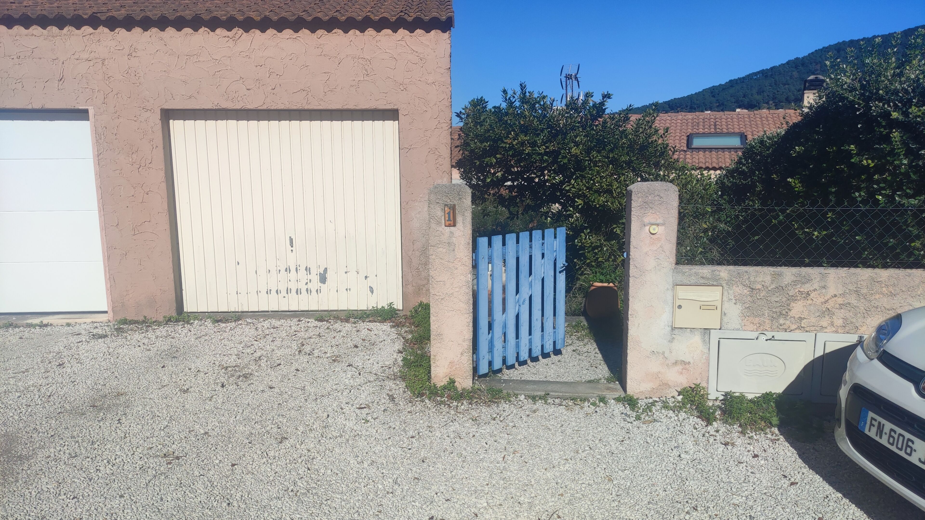 A building with a large garage door, a blue gate, and a car parked in front.