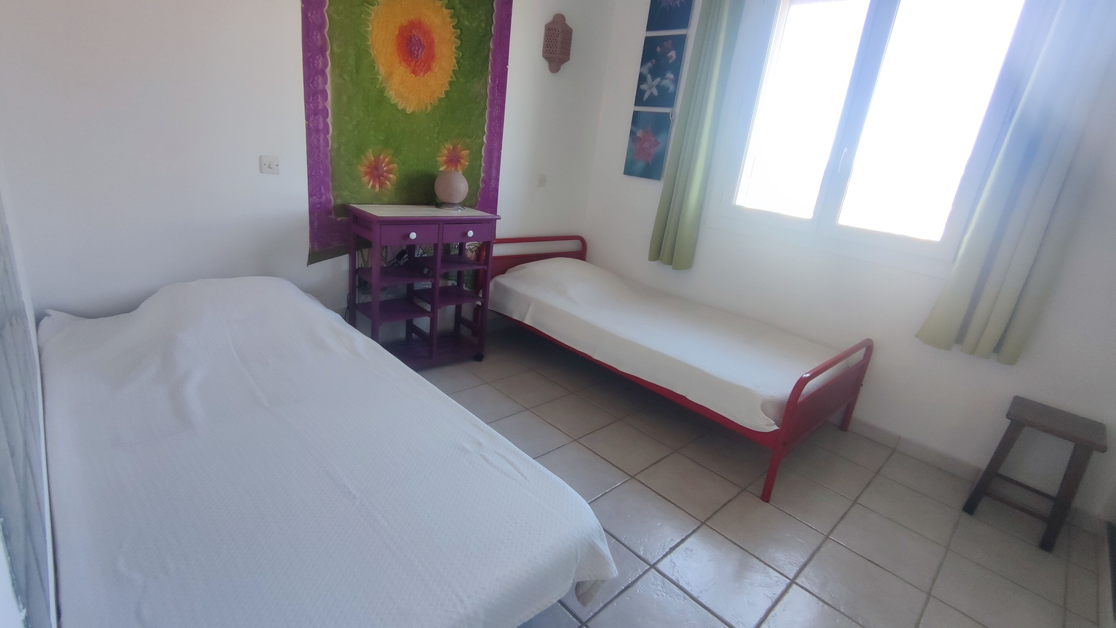 A room with two beds, a small table, a wall decoration, and a window with curtains.