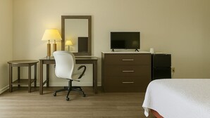 Habitación de hotel con cama, escritorio, silla, televisor, refrigerador y lámpara.