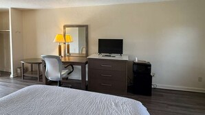 Habitación de hotel con cama, escritorio con computadora, una silla, lámpara y televisor.