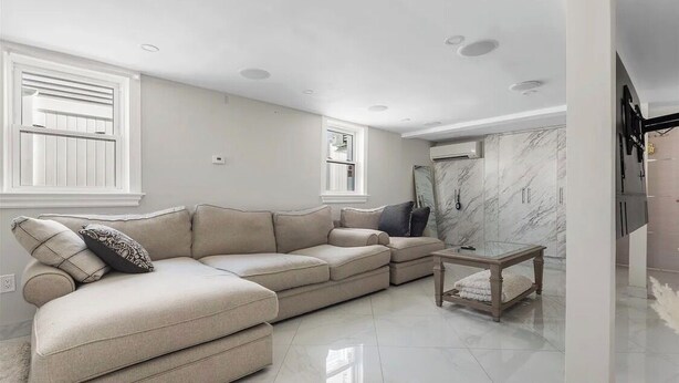 A living room with a beige sectional sofa, a glass coffee table, and a marble accent wall. - Howard Beach Luxury Perfect 3-bedroom 2-full bathroom apartment with Pool (Howard Beach)