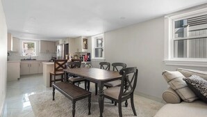 A modern kitchen with white cabinets, a dining table with chairs, and a sofa with cushions. - Howard Beach Luxury Perfect 3-bedroom 2-full bathroom apartment with Pool (Howard Beach)