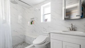 A bathroom with a shower, toilet, and sink, all in a white and marble design. - Howard Beach Luxury Perfect 3-bedroom 2-full bathroom apartment with Pool (Howard Beach)