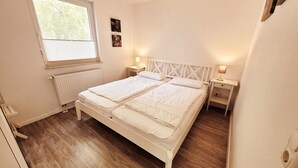 Une chambre à coucher avec un lit double, des tables de chevet, une fenêtre et un radiateur.