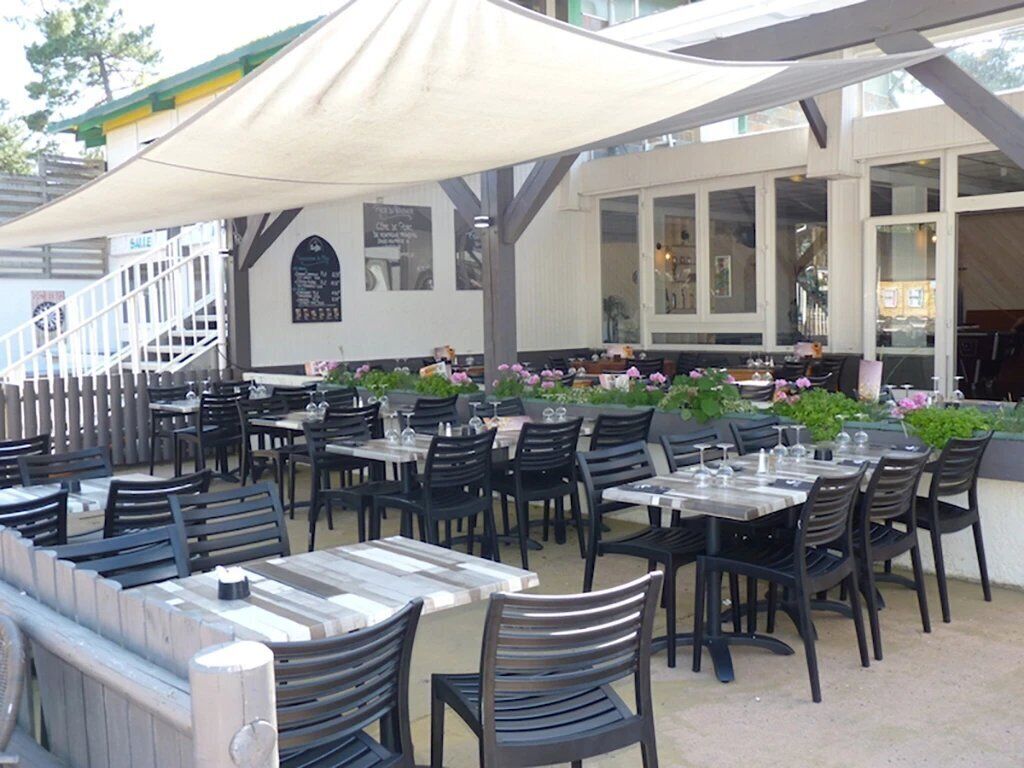 Un área de comedor al aire libre con mesas y sillas, un espacio de descanso cubierto y una escalera que conduce a un nivel superior.