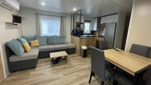 A compact living space with a sofa, a small table, a dining table with chairs, and a kitchenette. - Camping 4 étoiles - Parc aquatique - ccbfgac (Les Mathes)
