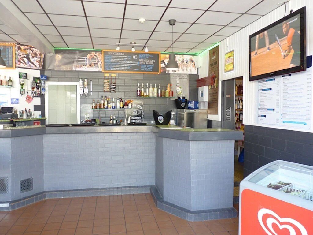 A bar area with a counter, shelves with bottles, a menu board, and a television screen.