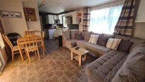 A compact living space with a sofa, a small table, a dining area with chairs, a kitchen area, and a window with curtains. - Camping 4 étoiles - Parc aquatique - ccbfgai (Les Mathes)