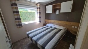 A bedroom with a bed, a window with curtains, a headboard, and built-in cabinets. - Camping 4 étoiles - Parc aquatique - ccbfgai (Les Mathes)