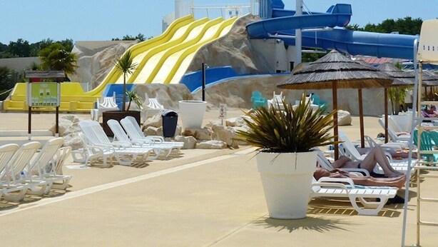 A beach with a water slide, lounge chairs, and a thatched umbrella. - Camping 4 étoiles - Parc aquatique - ccbfgai (Les Mathes)
