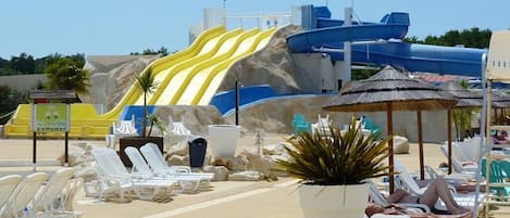 Una playa con tobogán acuático, sillas de descanso y una sombrilla de paja.