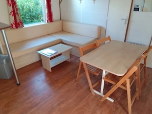 Una habitación con piso de madera, un sofá blanco, una mesita pequeña y un comedor de madera con sillas.