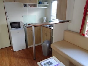 Una cocina compacta con microondas, estufa y fregadero, un pequeño cubo de basura y un sofá.