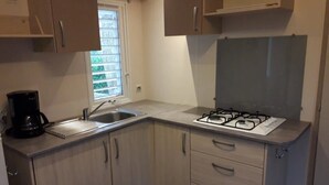 Una cocina compacta con estufa a gas, cafetera y ventana con persianas.
