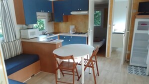 A compact kitchen with a dining area, a microwave, a stove, and a refrigerator. - Camping 3 étoiles - ccbfgdd (Neuvic)