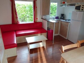 A compact kitchen with a red sofa, a small table, and a window with curtains.