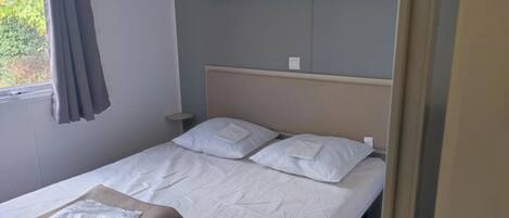 A single bed with white linens, a headboard, a bedside table, and a window with curtains.
