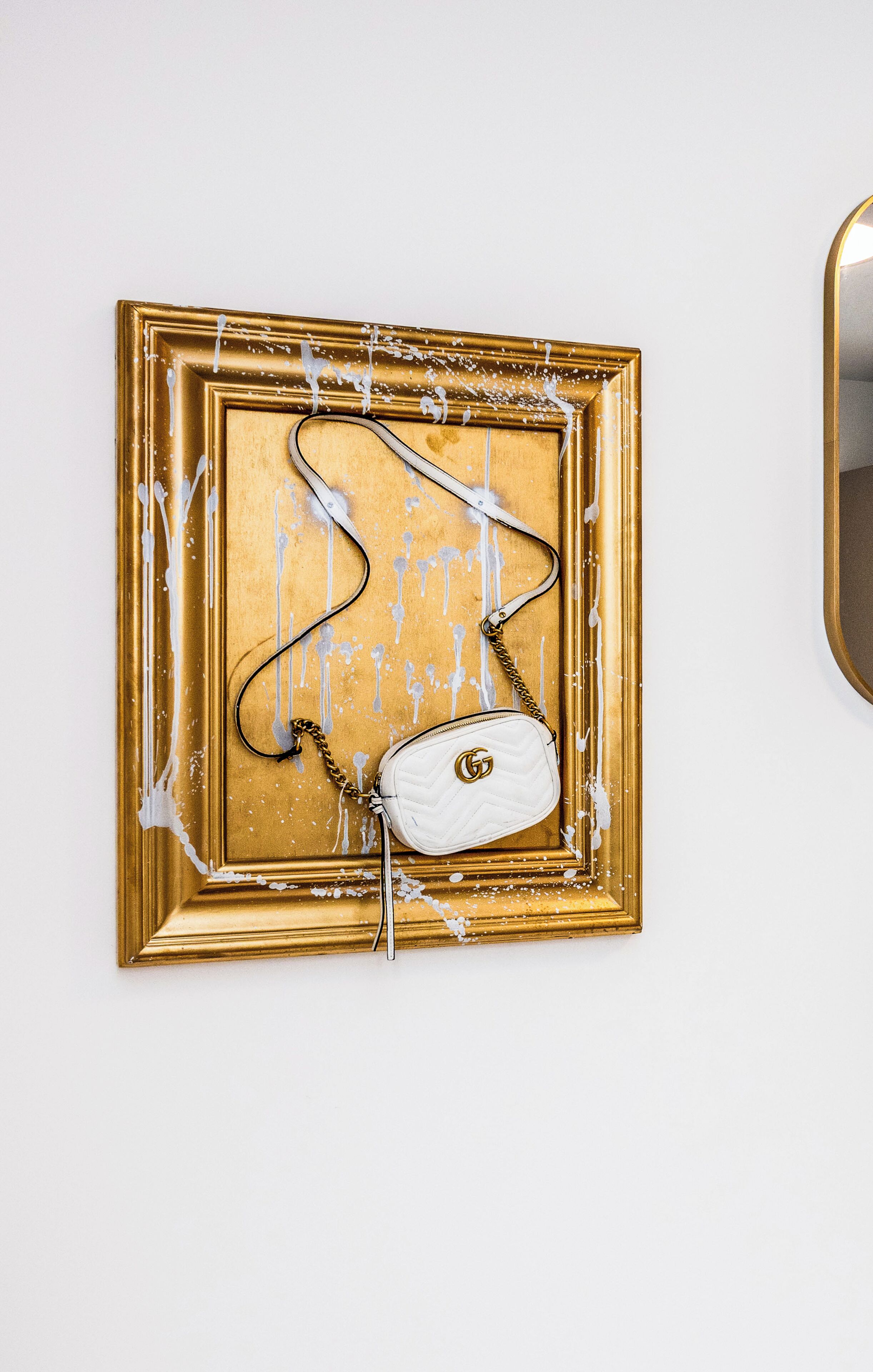 A white Gucci handbag on a gold-framed wall.