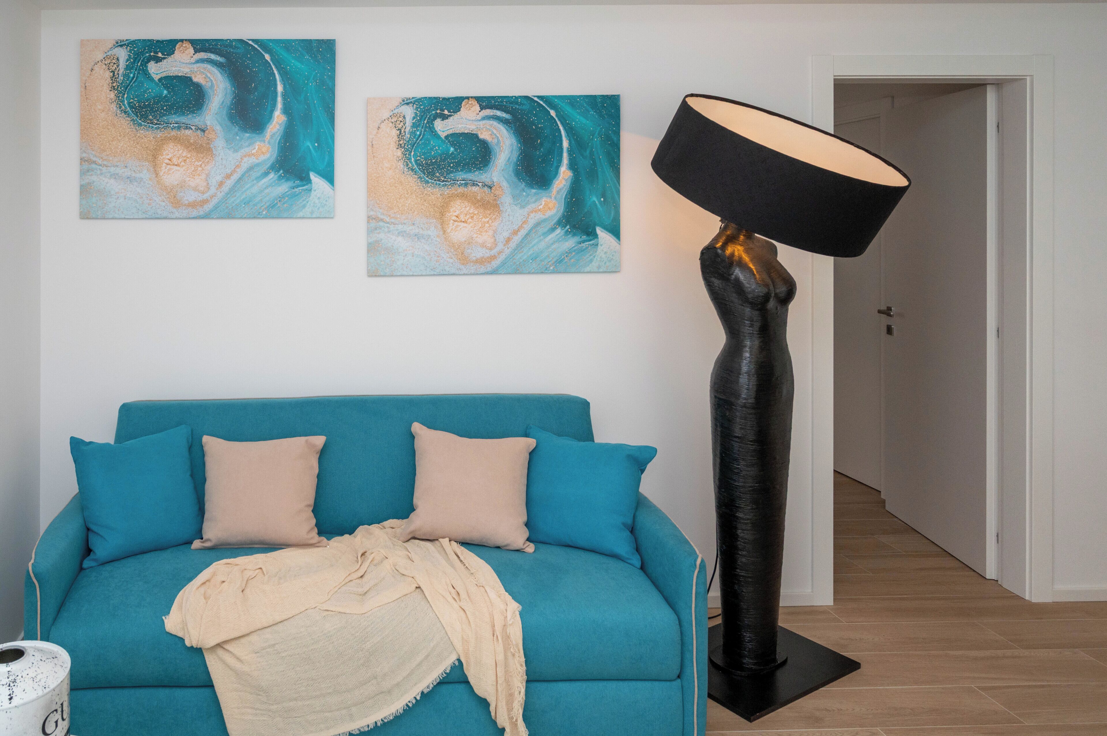 Um quarto com um sofá verde-água, um abajur preto e duas pinturas abstratas na parede.