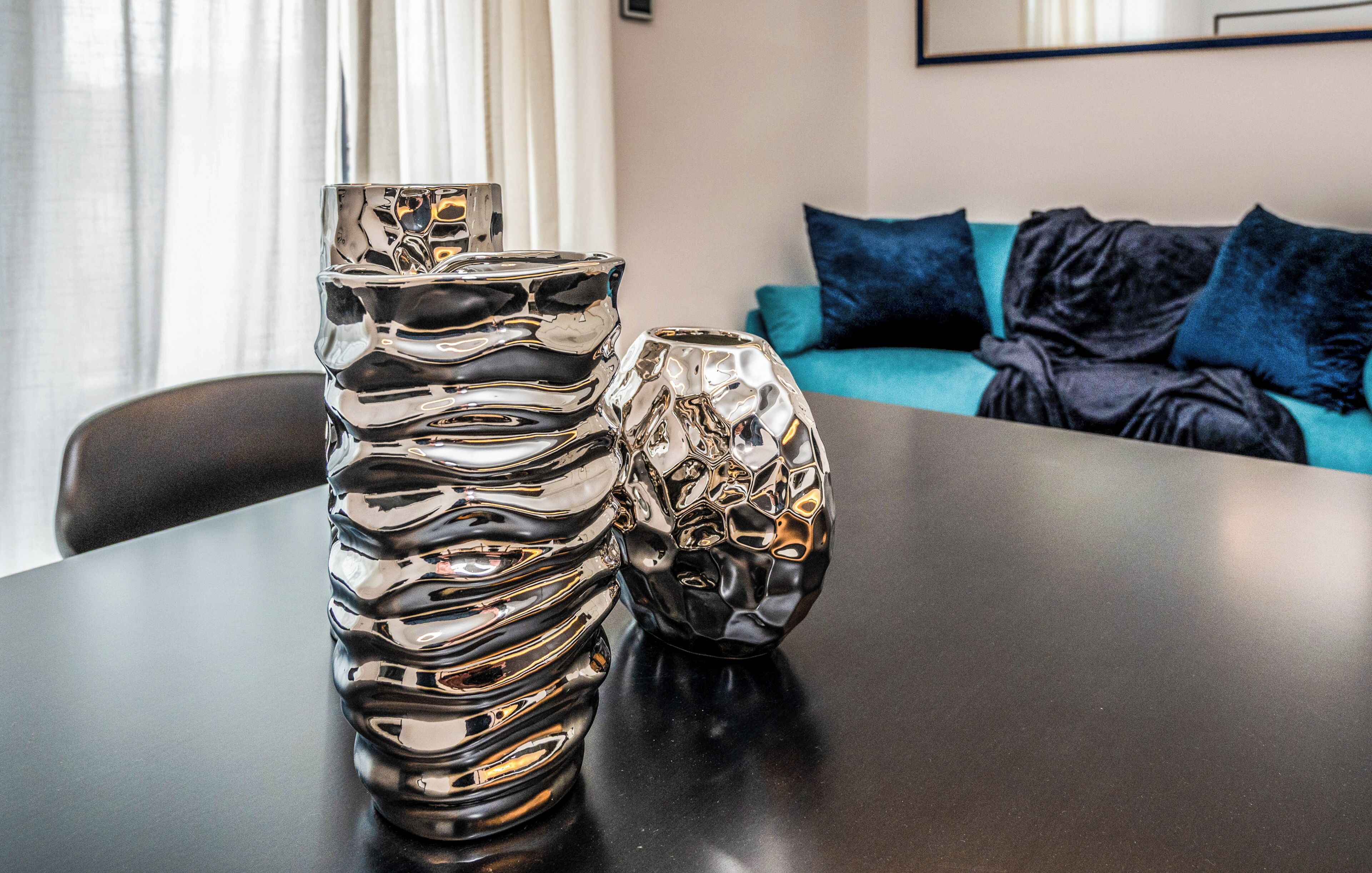 A table with two metallic vases and a teal sofa in the background.