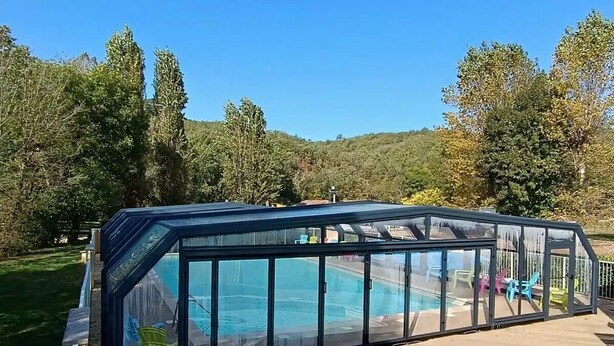 Ein Schwimmbecken mit Glasüberdachung, umgeben von einer Sonnenterrasse mit Liegestühlen.