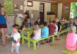 Ein Klassenzimmer mit Kindern, die an grünen Pulten sitzen, einer stehenden Lehrerin und einem Kind, das geht.